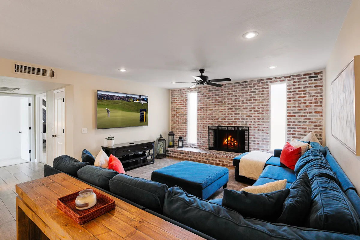 A spacious and inviting living room featuring a large sectional sofa, a cozy fireplace, a smart TV mounted on the wall, and a wooden coffee table. The mood is comfortable and relaxed, ideal for gathering with friends and family for movie nights or conversations.