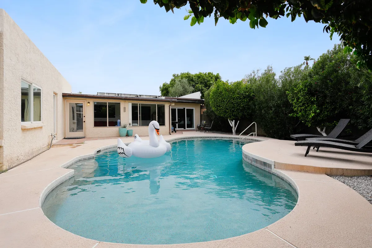 A playful exterior scene with a sparkling swimming pool, a large swan float, several lounge chairs, and the house’s facade in the background. The arrangement is designed for both sunbathing and lively pool games, underscoring a fun, group-friendly mood.