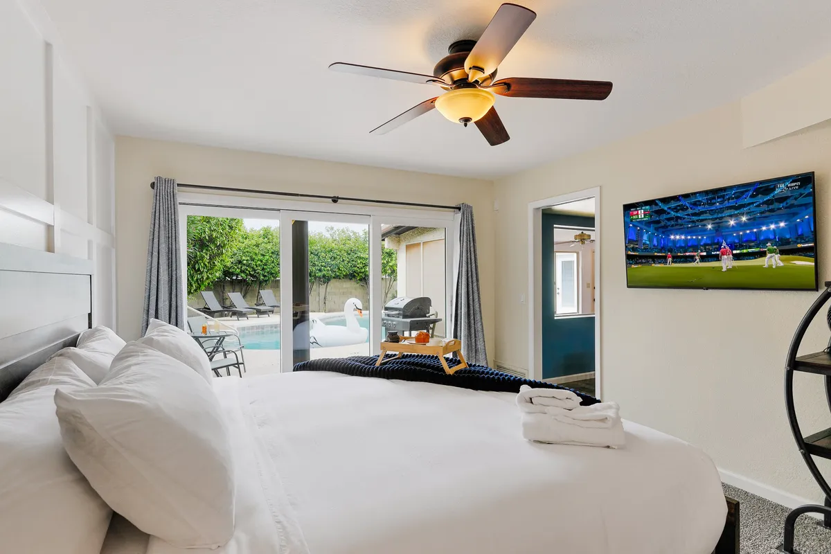This image captures a spacious bedroom featuring a comfortable bed, television, and sliding glass doors that lead directly to the pool area. Natural light streams through the doors, creating a bright and inviting ambiance.