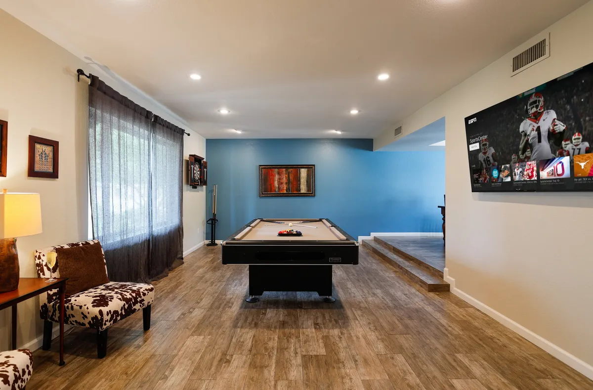 This scene features a pool table as the centerpiece, a large television for game-watching, decorative artwork, and a comfortable seating area arranged for social interaction. The playful mood is reinforced by the inviting setup, perfectly suiting both competition and relaxed lounging.